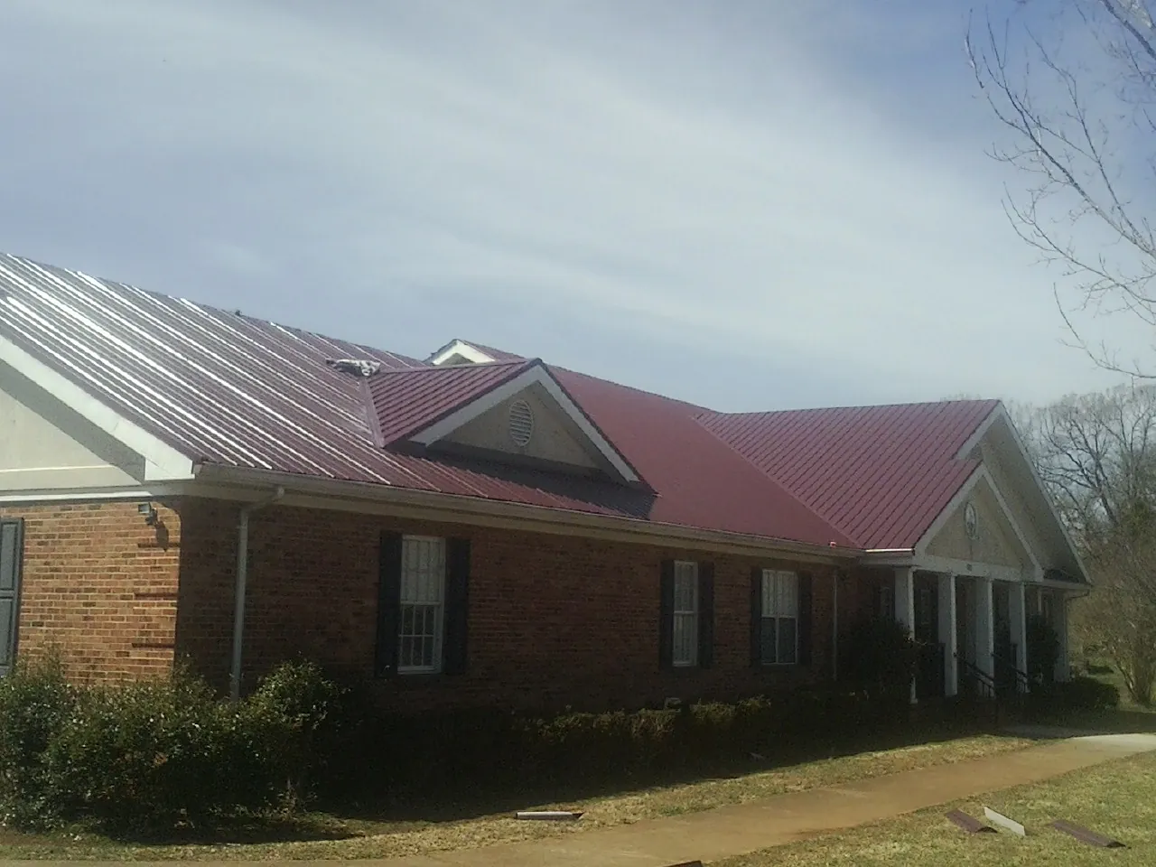 Red metal roof with gabled entries on a long brick building, from a Hail Damage Roof Repair job in Graniteville