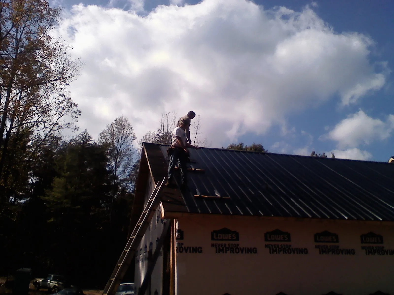 Roofer fastening dark metal panels high against a cloudy sky, from a Roof Inspection job in Graniteville
