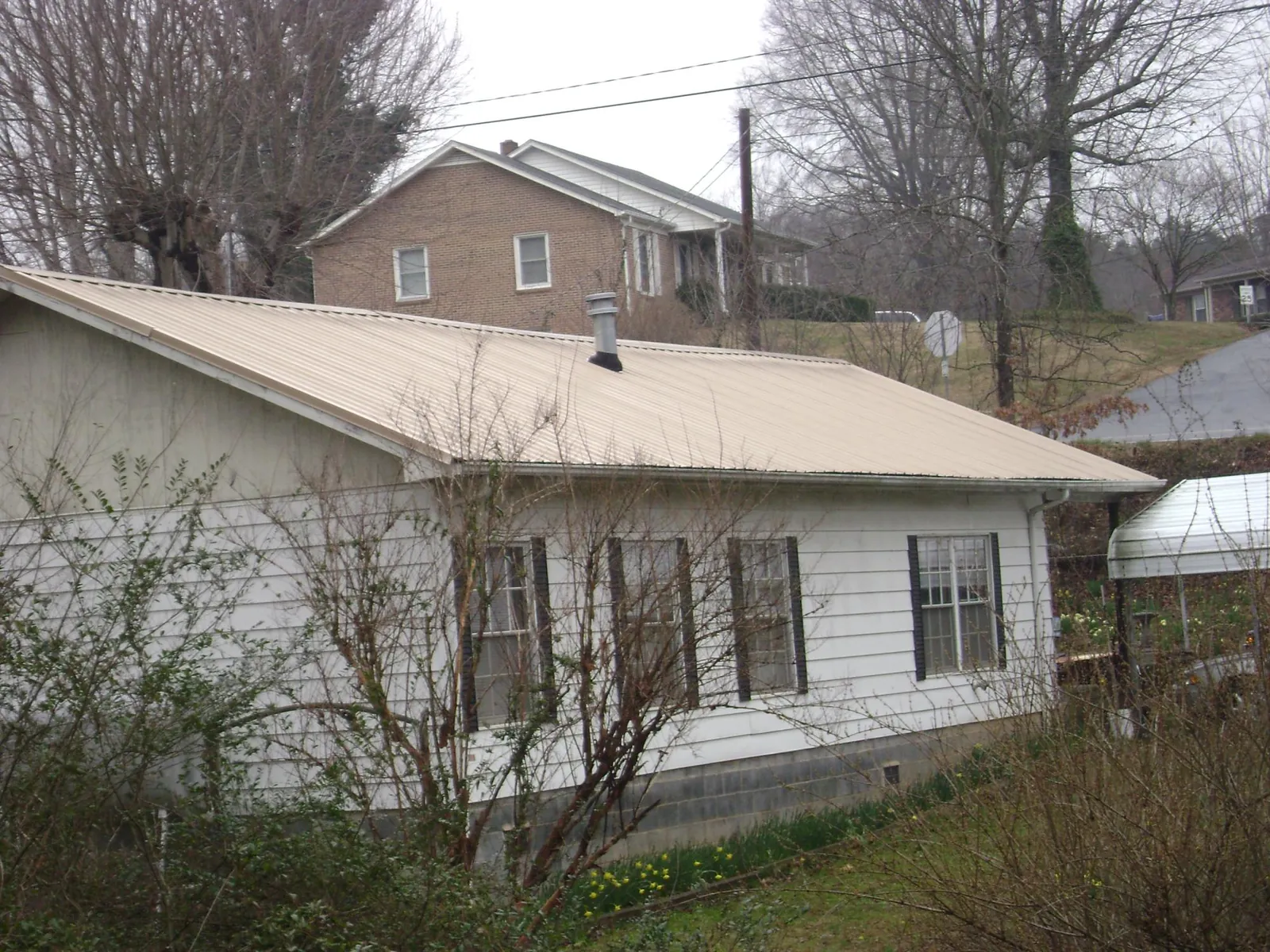 Tan metal roof on a white sided house set into a hillside — Commercial Roofing by Roofing Brothers in Graniteville