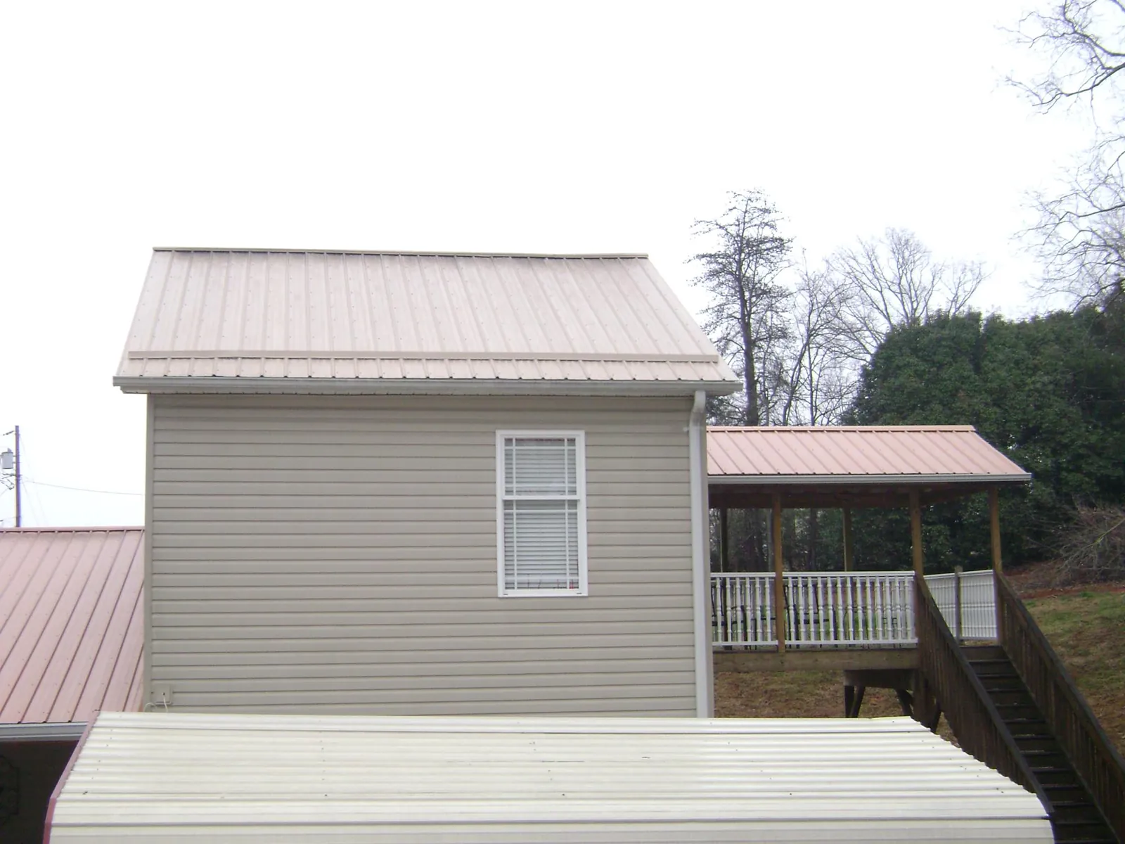 Tan metal roofs on a two story addition and attached porch, from a Roof Replacement job in Graniteville